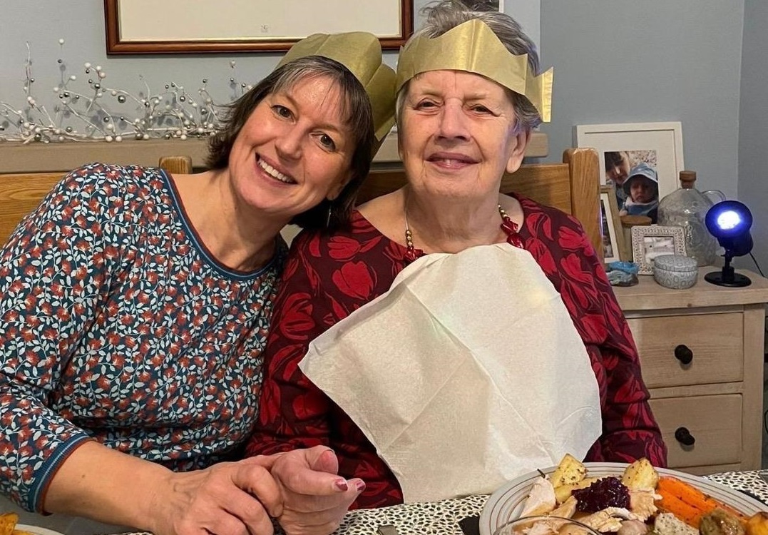 Katie and Lesley in Christmas cracker hats sat at a Christmas meal