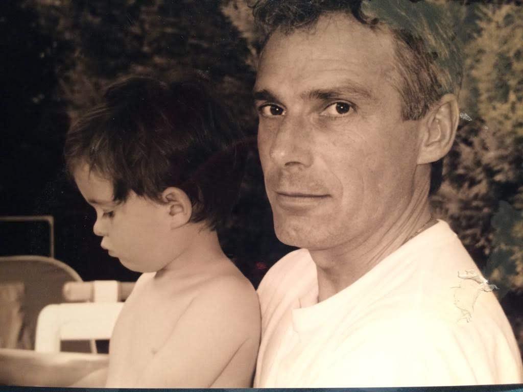 Lauren Hughes as a young child is sitting on her dad Chris' lap. Chris looks at the camera. The photo is an old sepia family photo