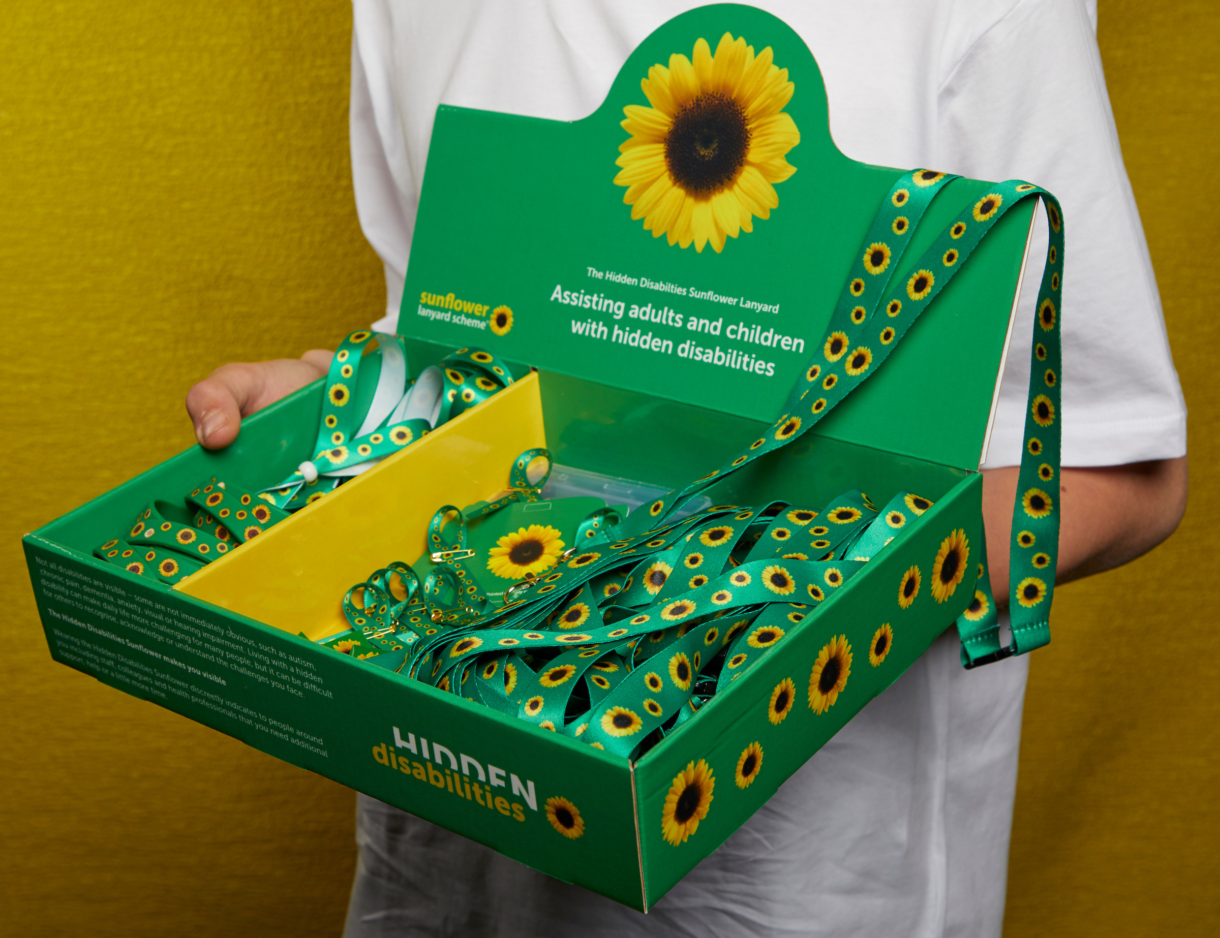 A person wearing a white t-shirt holding a box of sunflower lanyards