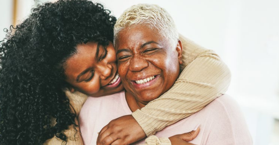 A young woman embraces her mother lovingly, both women are grinning.
