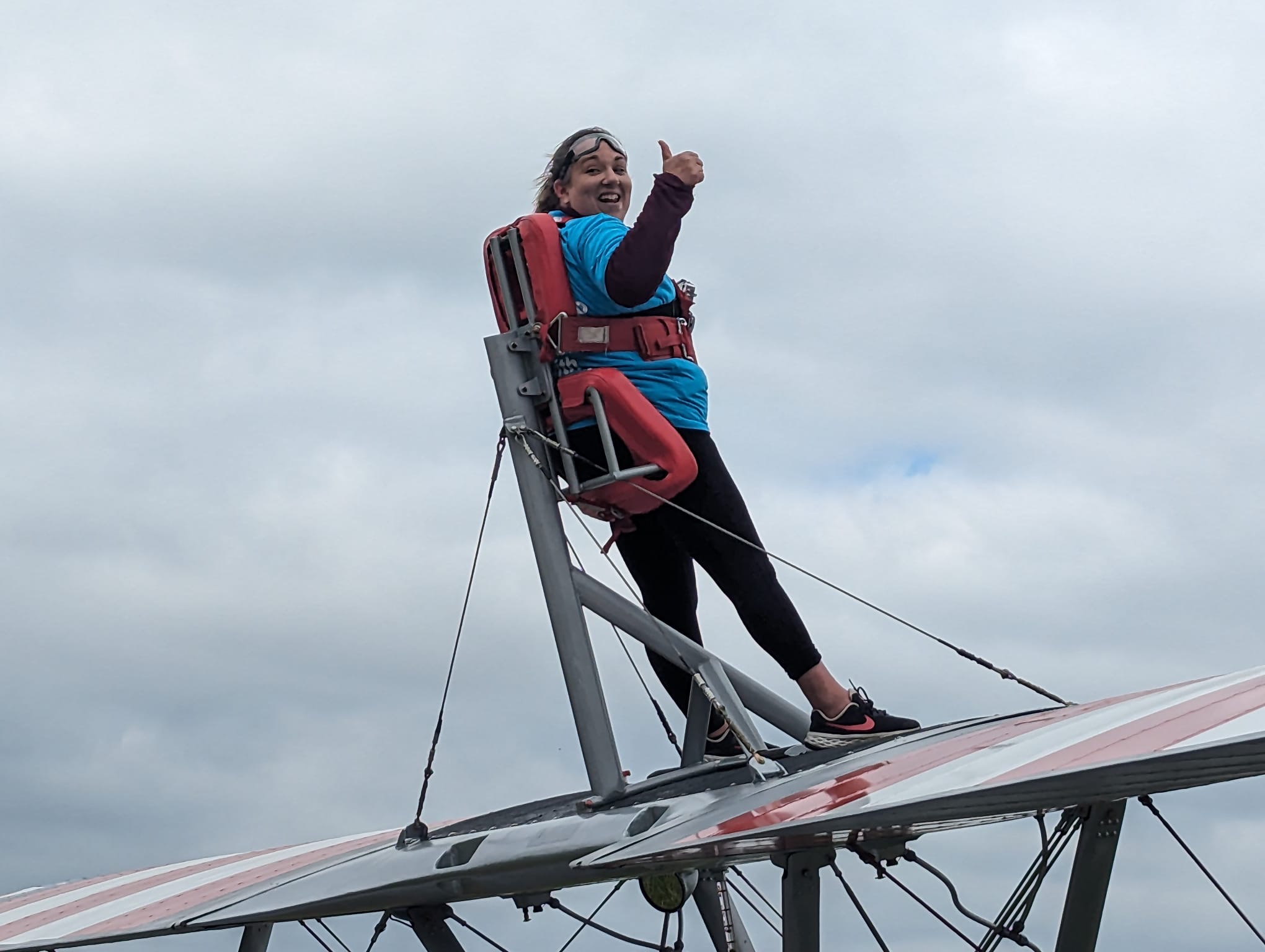 A woman stands on a small aeroplane wing, strapped to a safety device