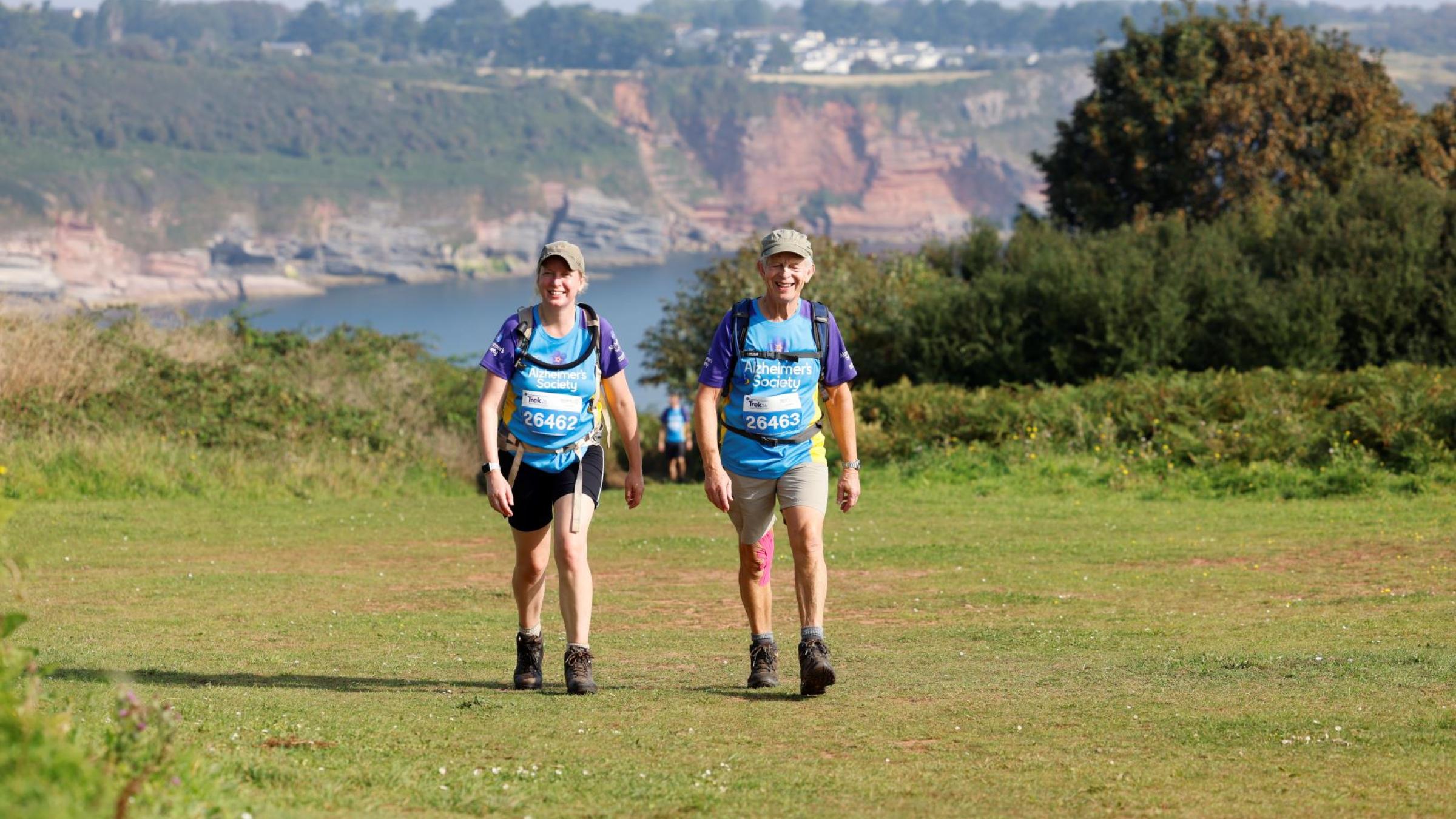 2 trekkers walking in the sun on a coastal path