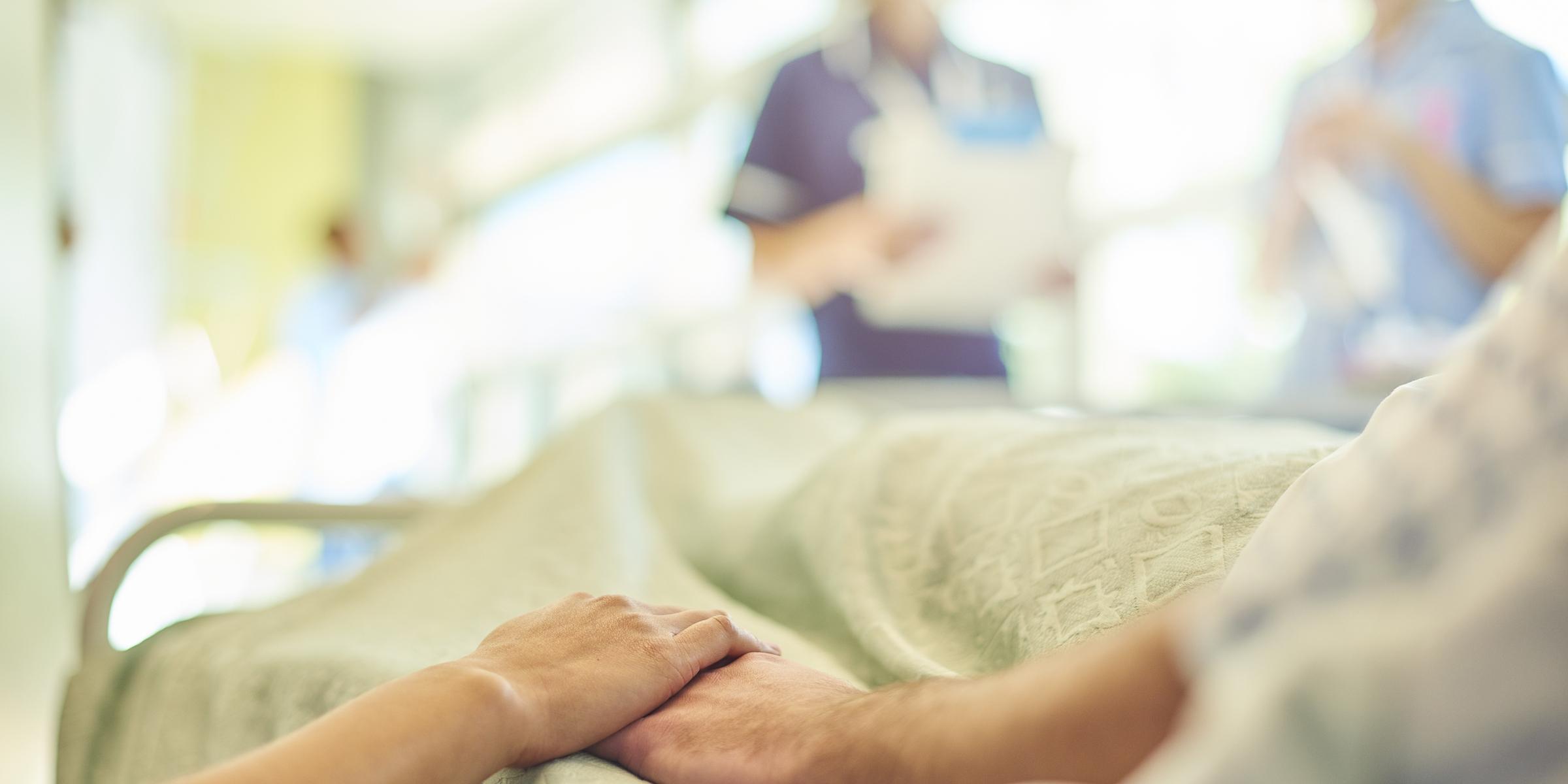 Holding a hospital patient's hand, with nurses talking in the background