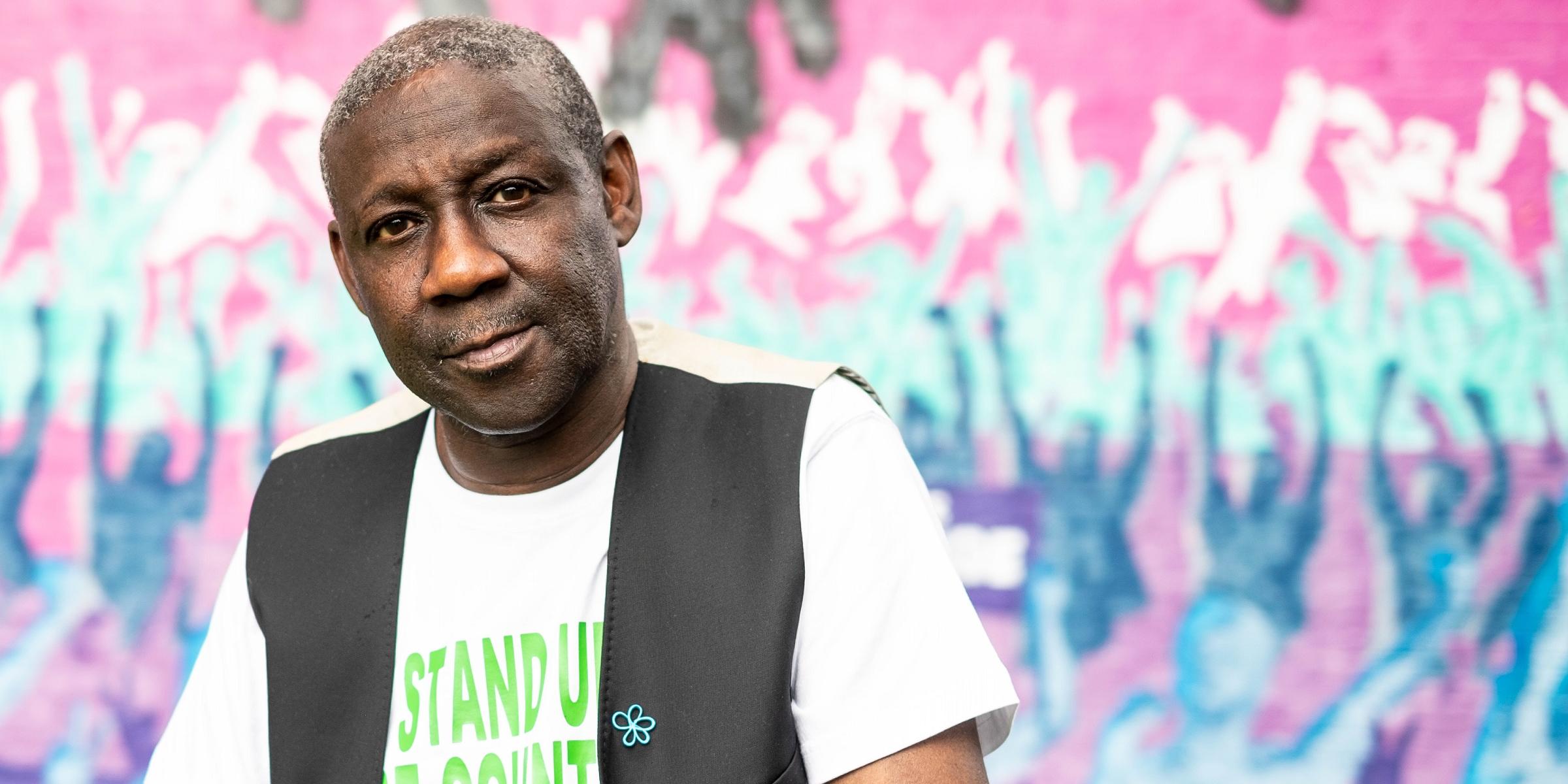 Ronald Amanze stands in front of wall of graffiti 