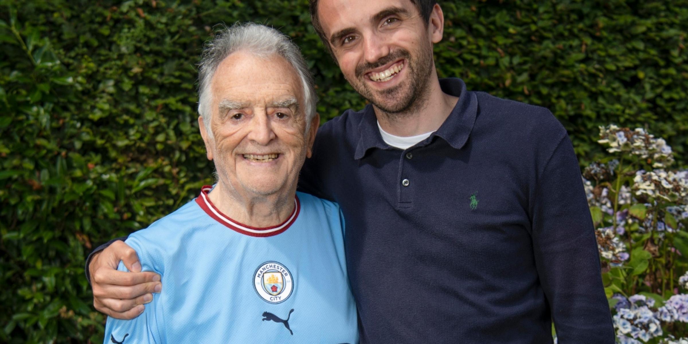 Charlie with his arm round Barry, his grandad, who is wearing a Manchester City football shirt