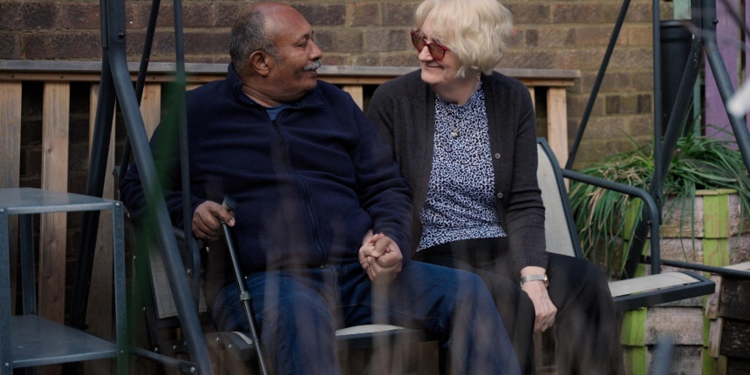 Ananga and Jo sit on a swingchair while holding hands and looking at each other