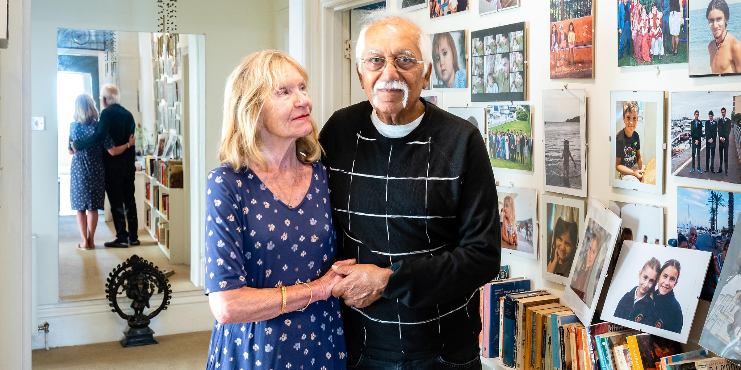Maggie and Rashmi Paun stand in their home next to a wall of family photos