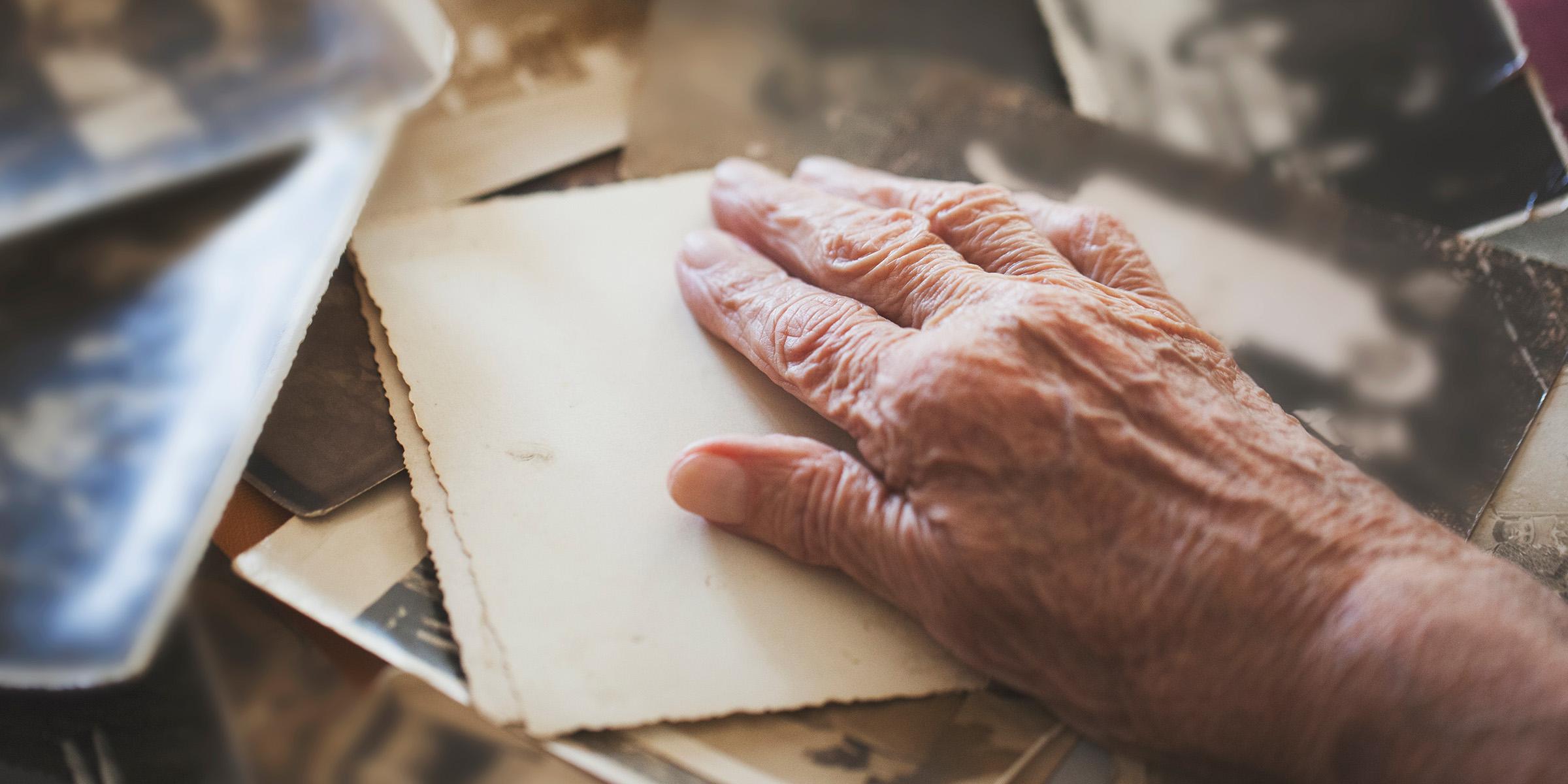 An older person's hand on top of some photographs, which are face down.