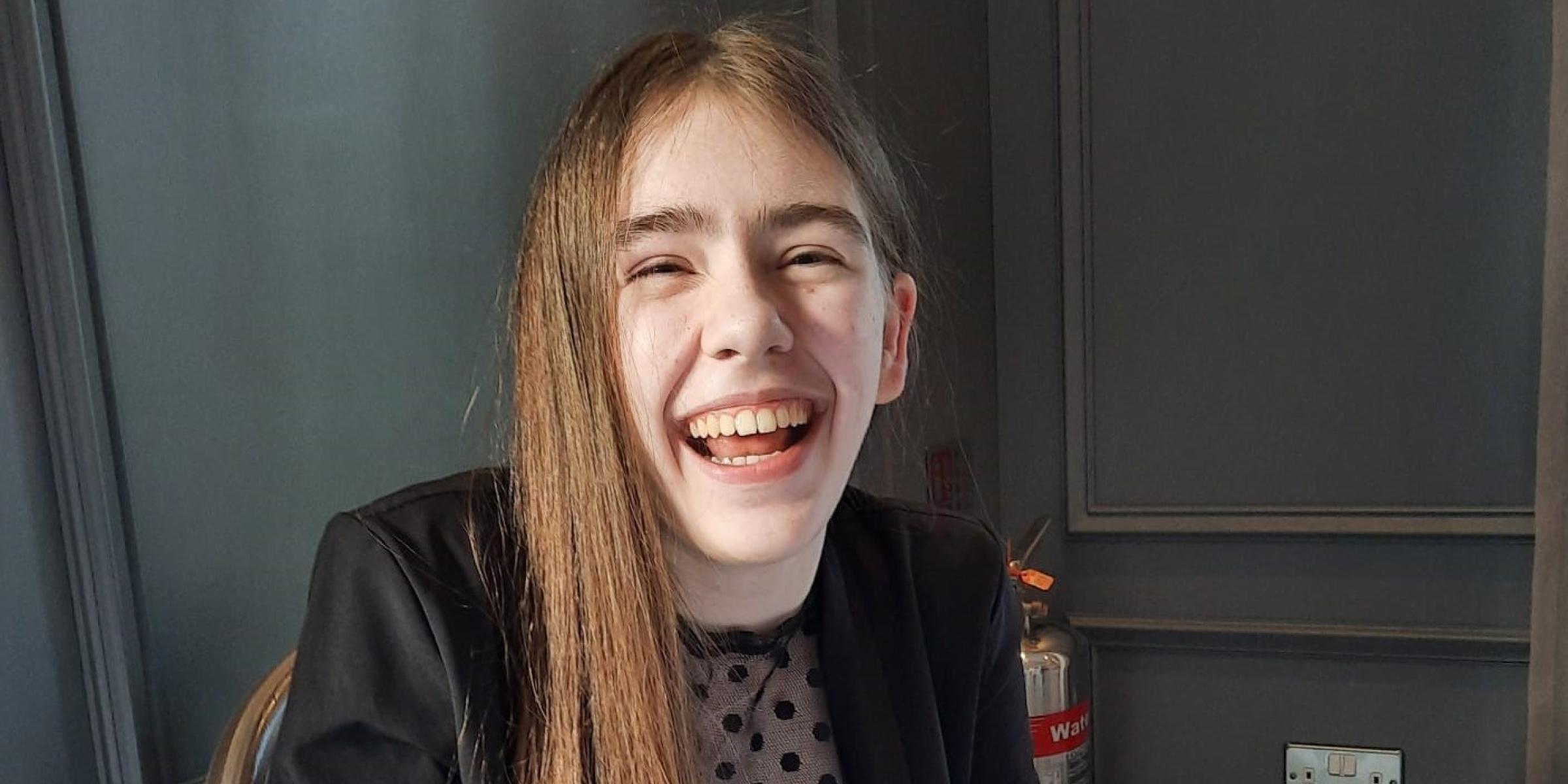 Eden is wearing a black blazer and a dotty black top. She has long brown hair and is smiling at the camera