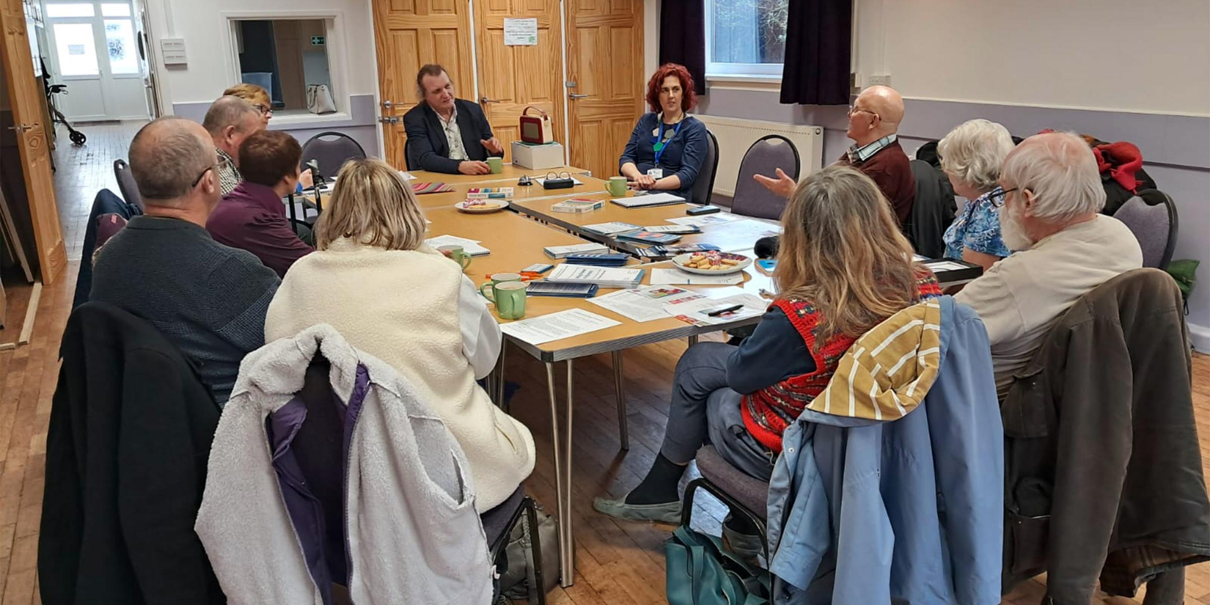 Group of people sat around table listening and looking at music player