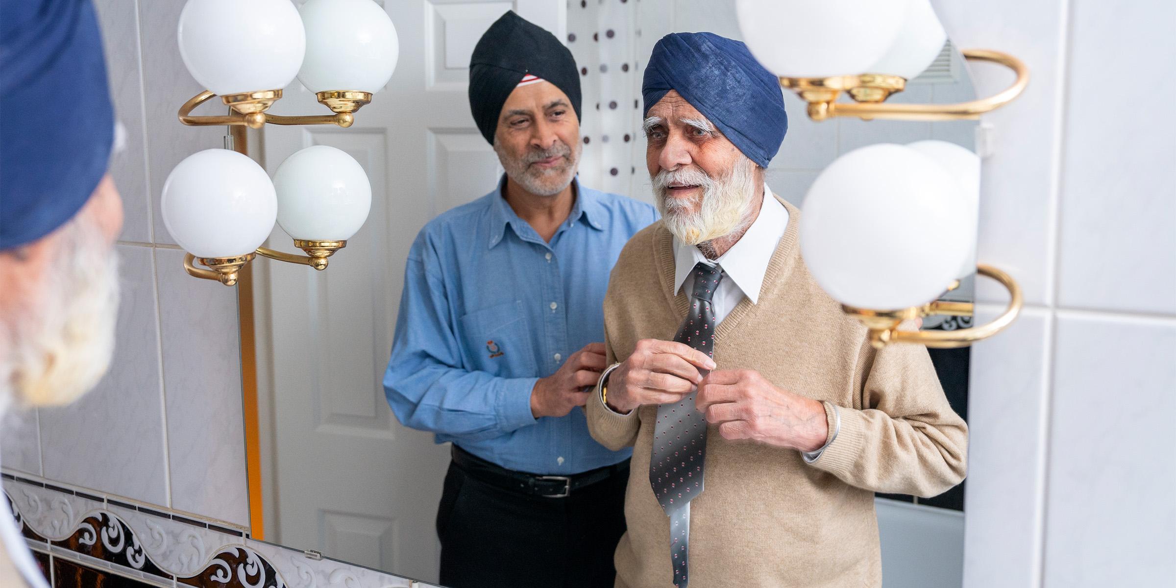 Dalwinder helping his dad Gurdev with his tie while stood in front of a mirror