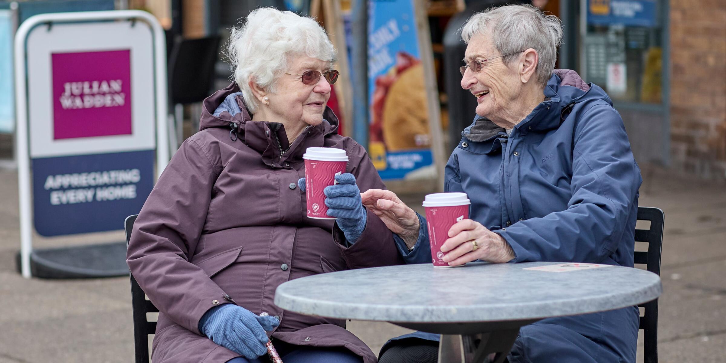 Two women drinking coffee outside around a table