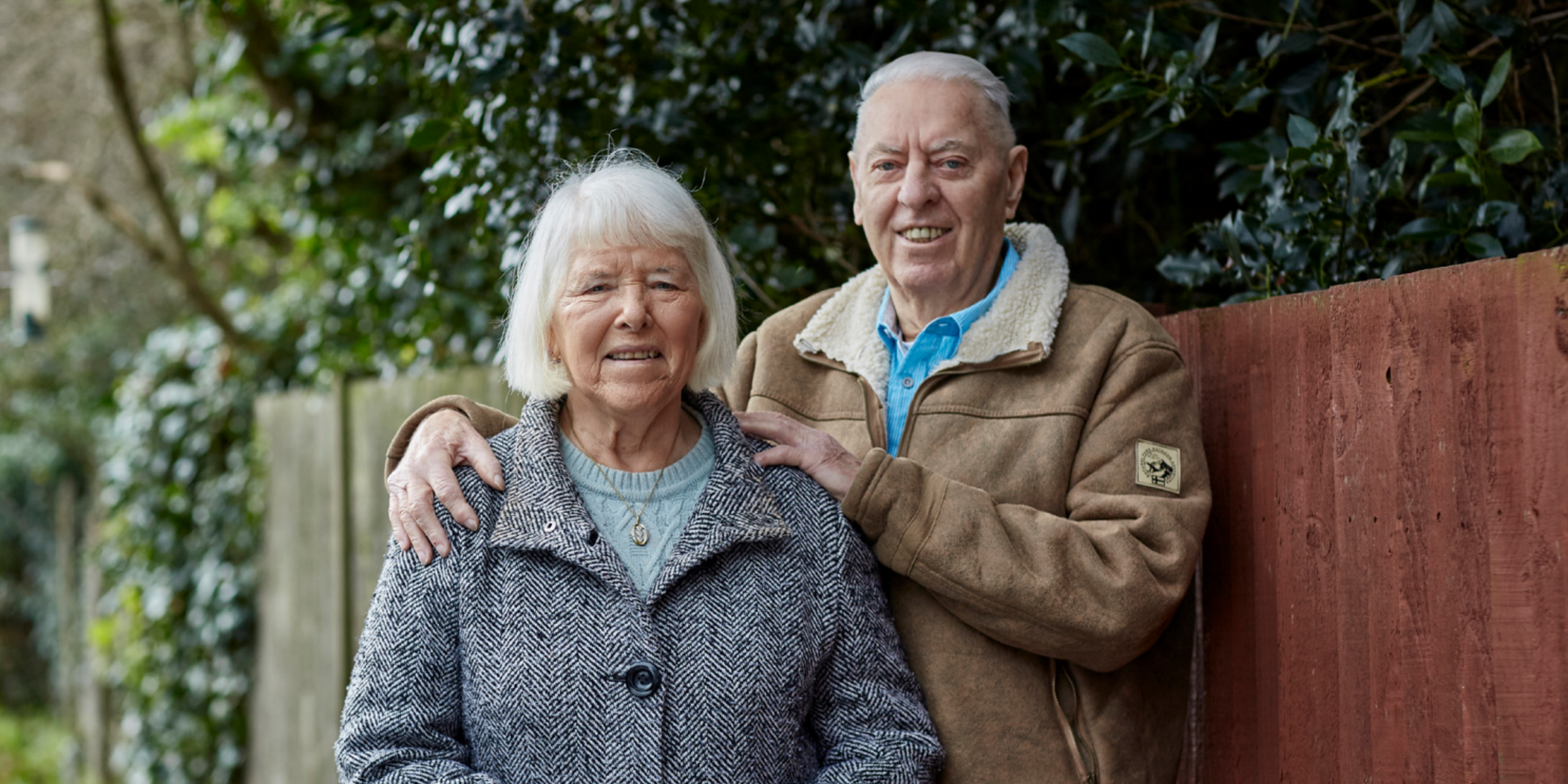 A man and woman stand smiling outside in winter coats