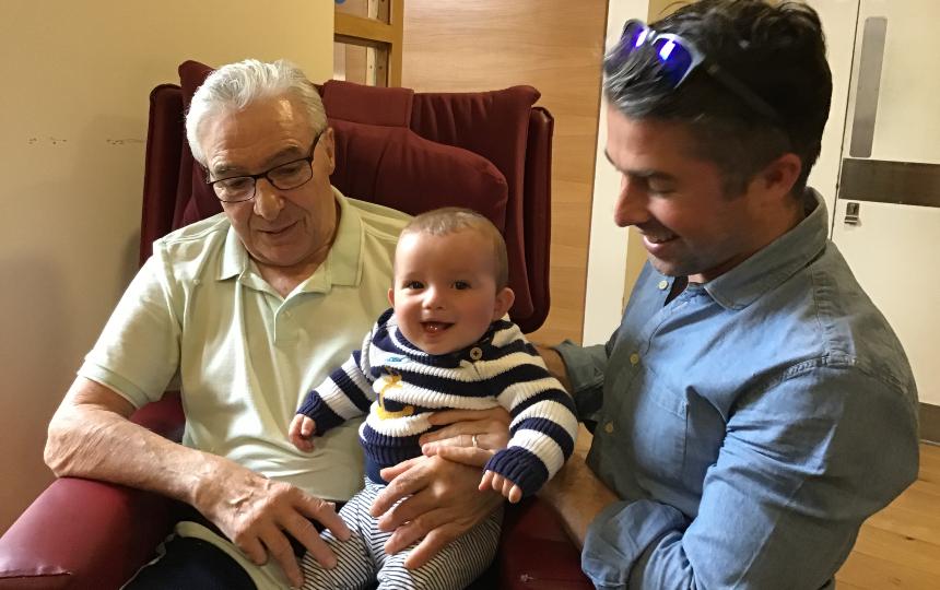 Charlie with his dad, who sits in an arm chair, holding a smiling baby