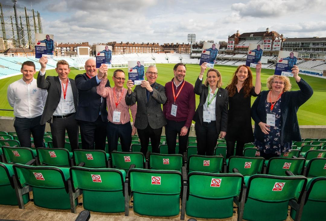A group of people at a sports ground holding up the Dementia friendly sports guide