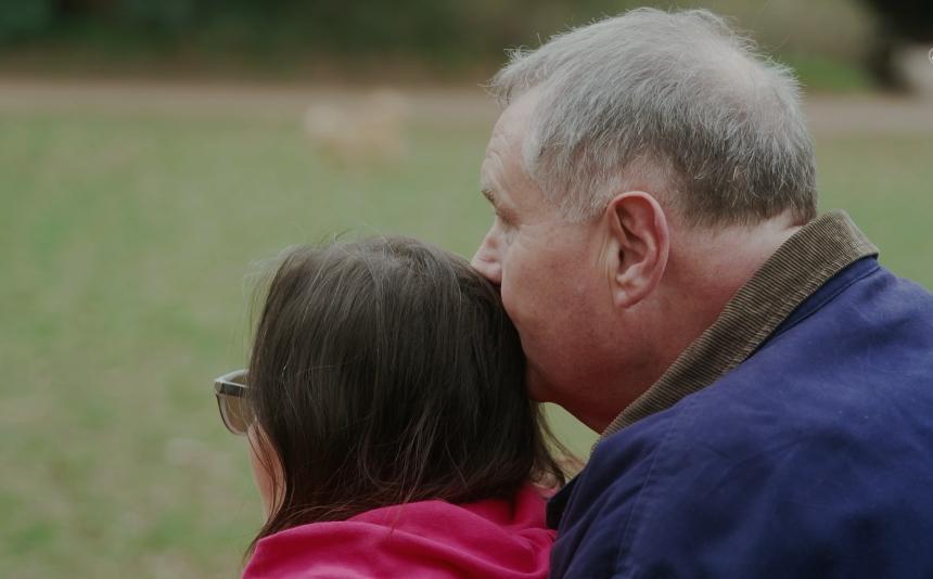 Bill hugging Jo, kissing the back of her head while she looks forward