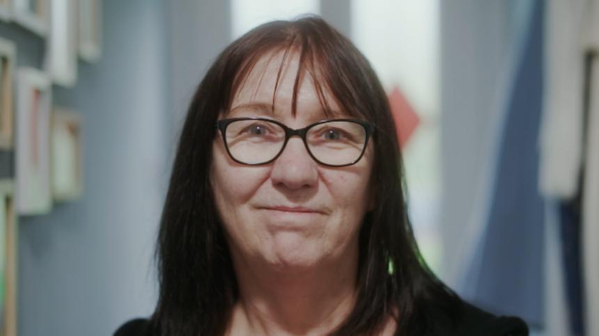 Gina standing in her hallway facing the viewer and smiling