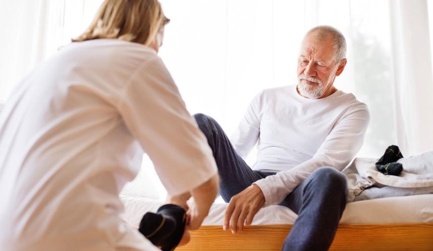 An older man is being helped by a woman to put on socks