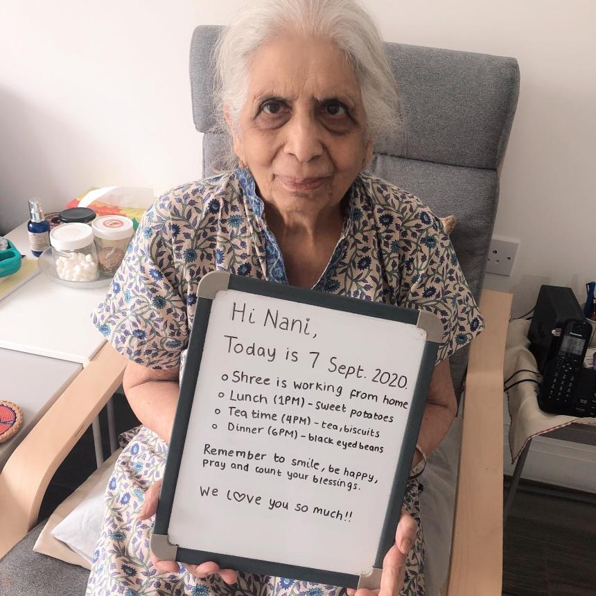 Shree's grandmother Varda holding her whiteboard to-do list for the day and smiling