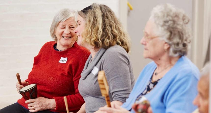Three people with percussion instruments laughing as they take a break from singing