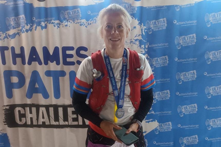Judith wearing her medal in front of a sign saying Thames Path Challenge