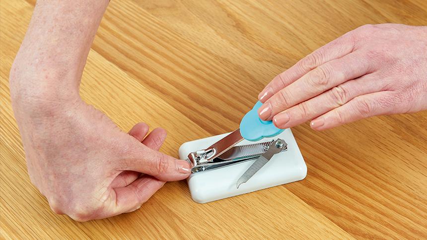 Someone's hands. They are cutting their thumbnail with a tabletop nail clipper