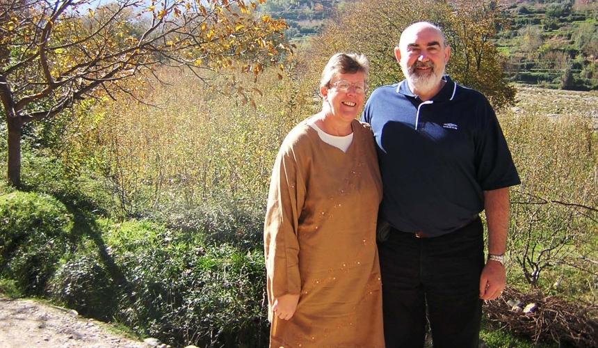 Ian and his wife stand in front of an open field in the sunshine
