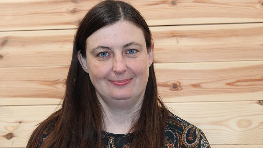 A head and shoulders picture of Cath Wohlers, looking at the camera smiling against a slatted wooden background