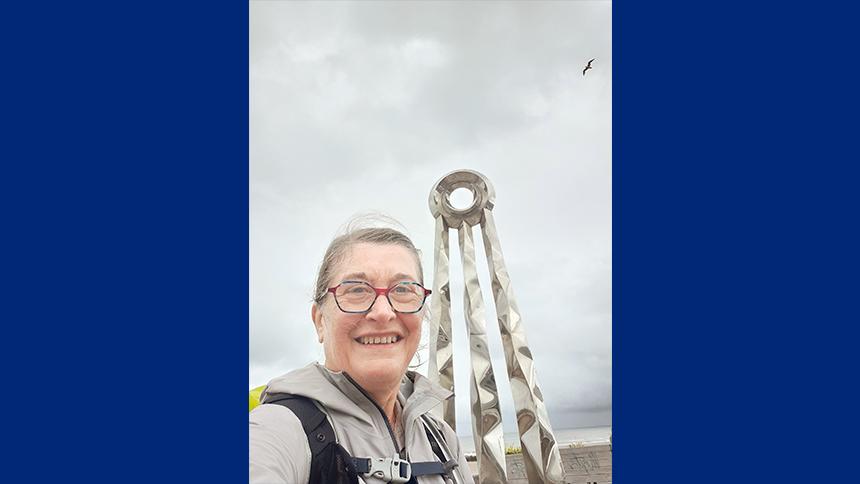 Jane Buckels stands outside on a grey day wearing a grey jacket and backpack, during her Offa's Dyke Path walk. She is smiling at the camera