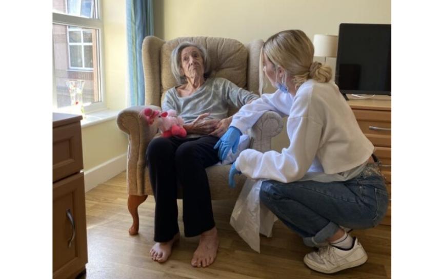 Grace crouches down to be level with her Nanna who is sitting in an armchair