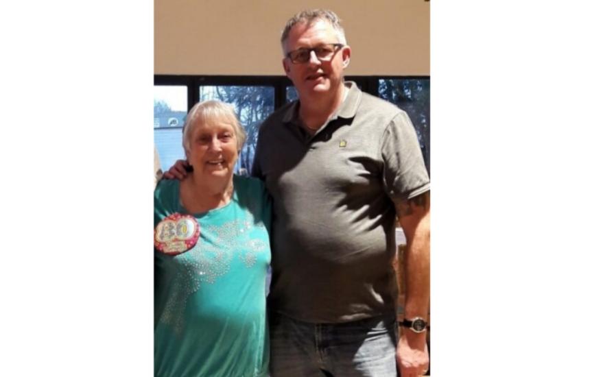 Peter with his arm round Doreen. She is wearing a badge that says 80