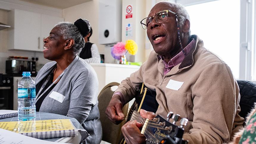 Man playing guitar and singing at Sheffield Memory Hub while woman sings behind him