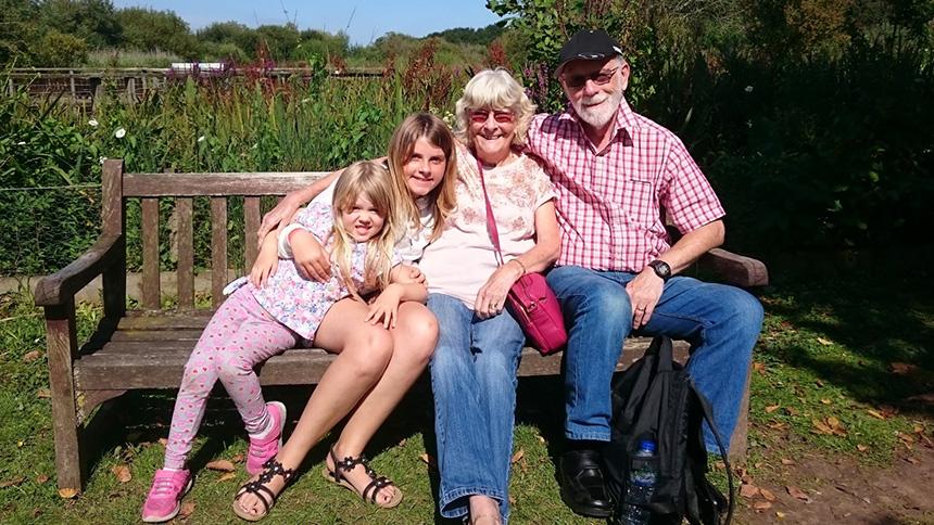 Brenda and her husband sat on a garden bench with two of their granddaughters