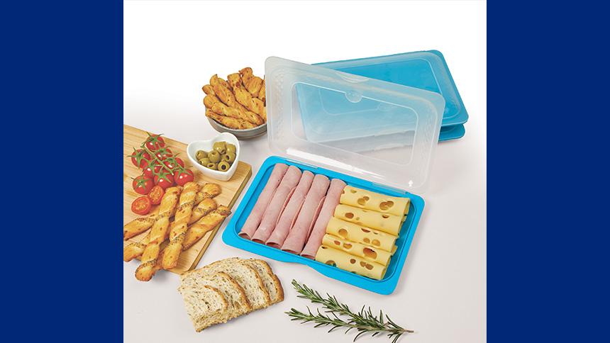 Opened up snack tray stacker containing cold meat and cheese next to a bread board
