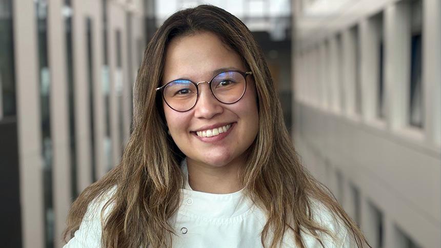 Melissa Parra Torres smiling wearing lab coat and stood inside university building