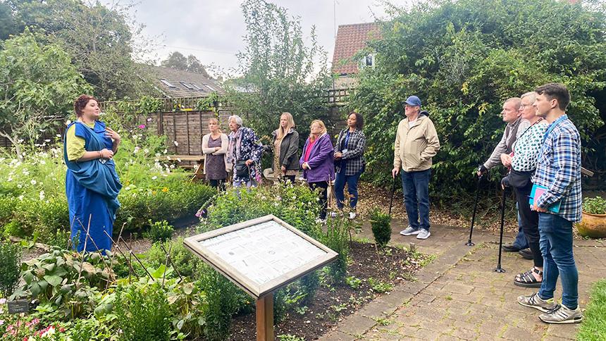 Project participants stood in a row in a garden looking at a woman wearing a historic costume