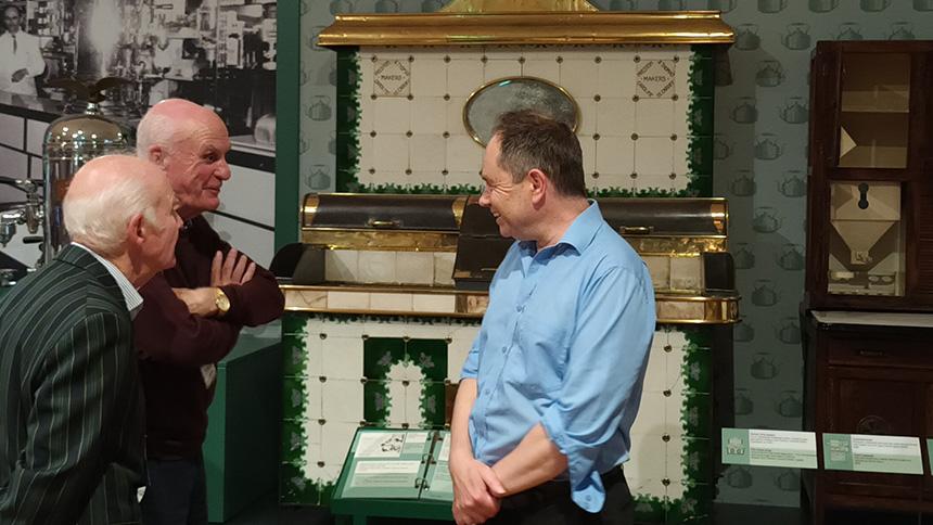 Two smartly dressed men talk to another man in a blue shirt in front of museum exhibits 