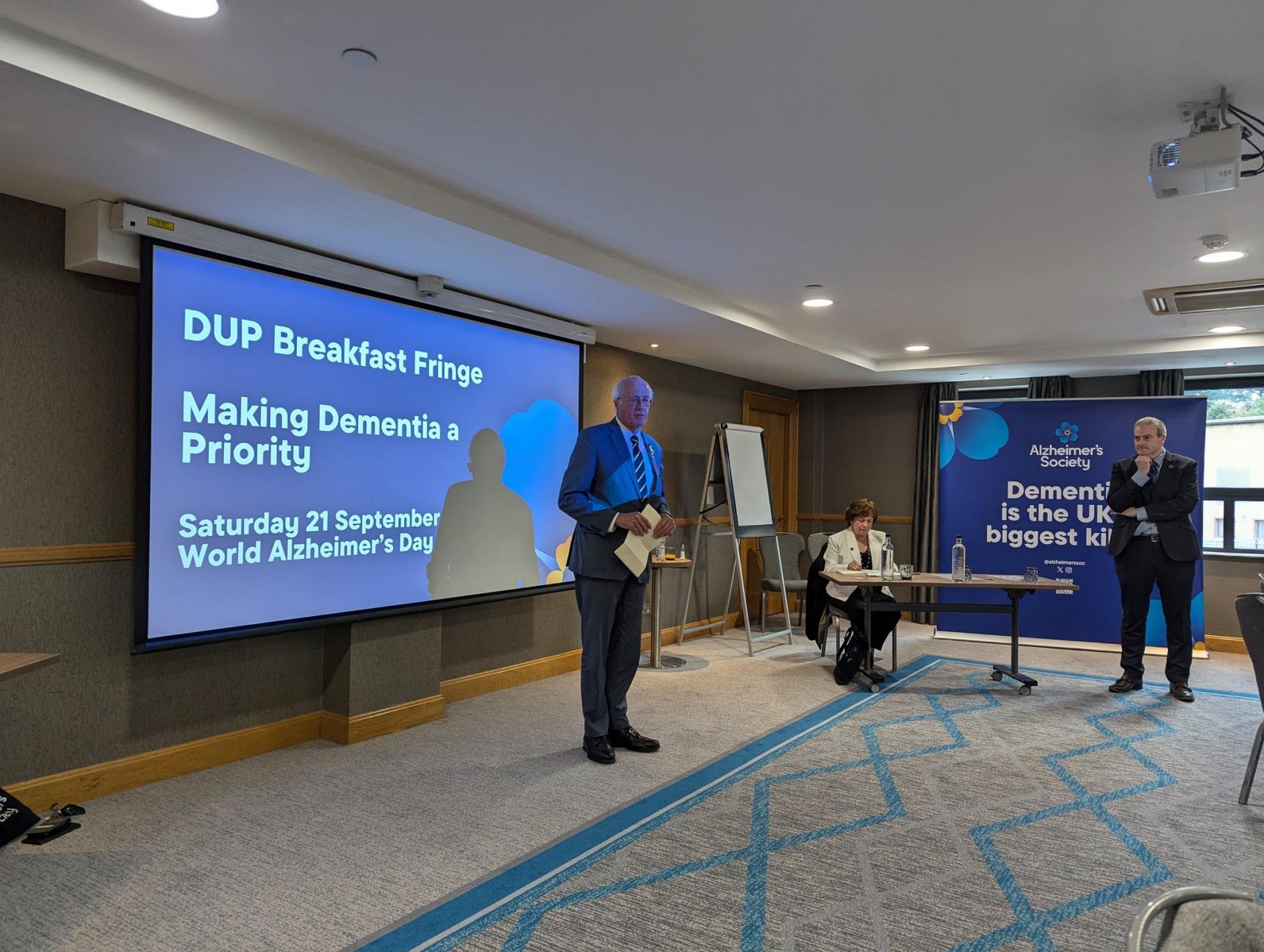 A man stood in front of a projector screen with Alzheimer's Society branding.