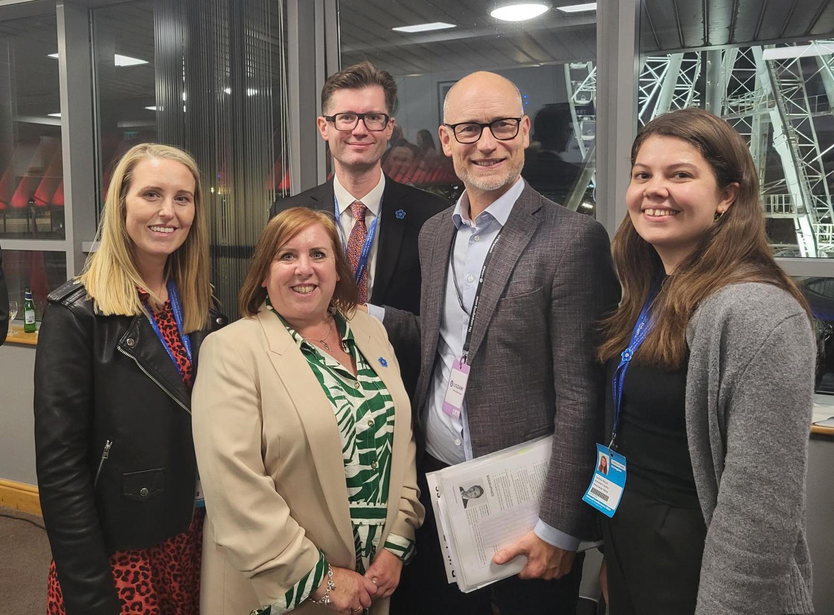 Three women and two men smiling at the camera.