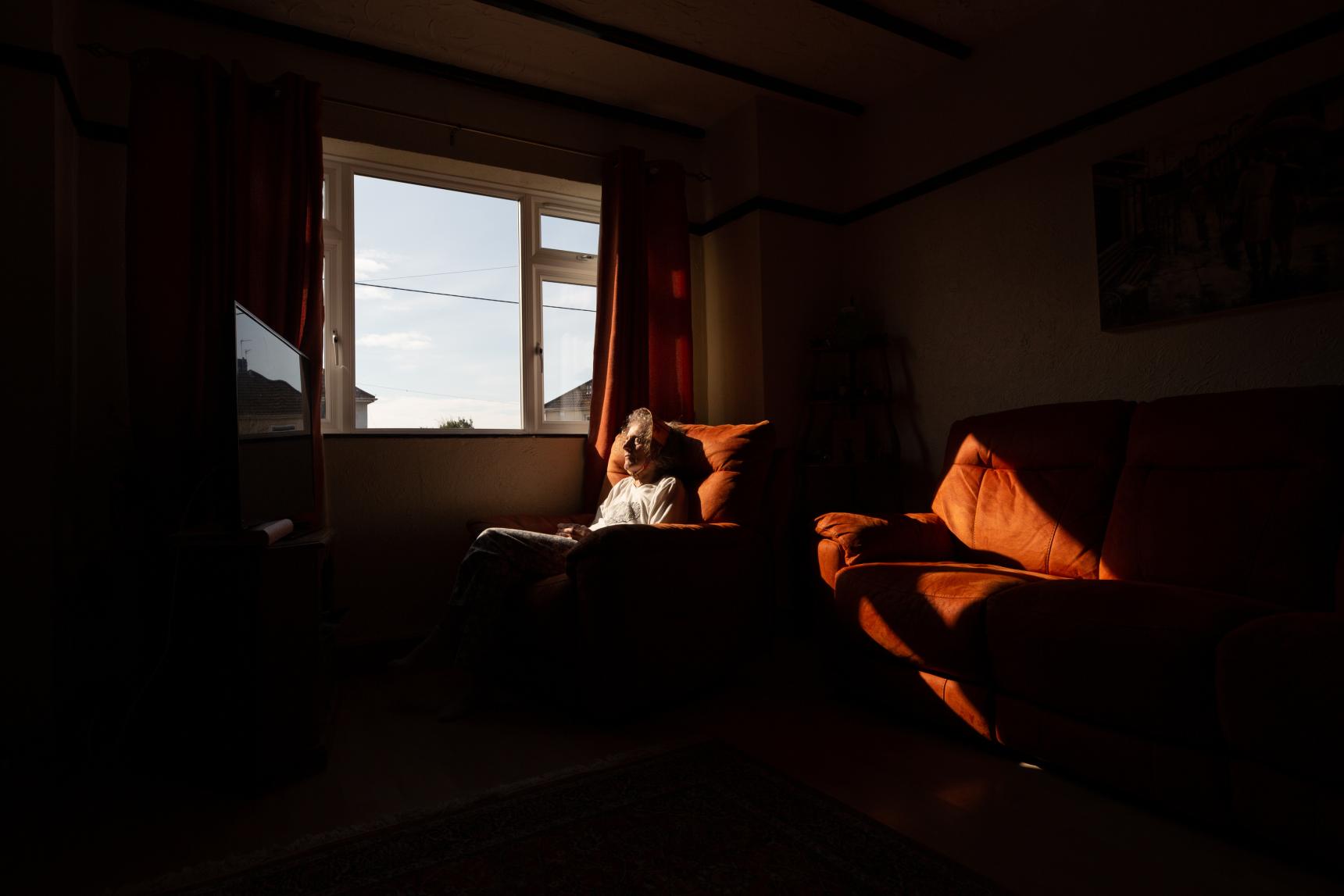 Sunlight comes in through a window. An elderly woman warms her face in the light