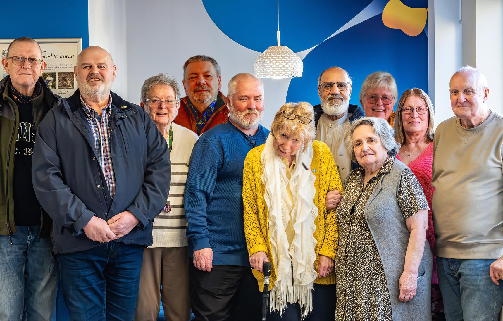 A group of older men and women stand together, smiling at the camera.