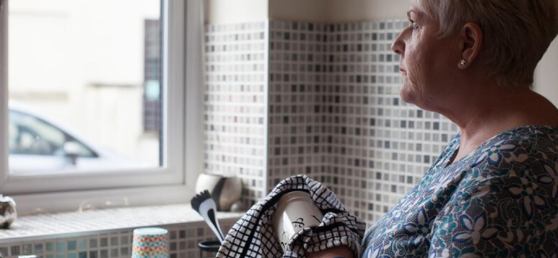 A woman gazes out of the window whilst drying a mug with a tea towel.
