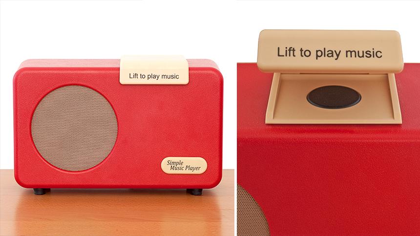 Simple music player in red sat on table, a lid that says 'lift to play music' is lifted