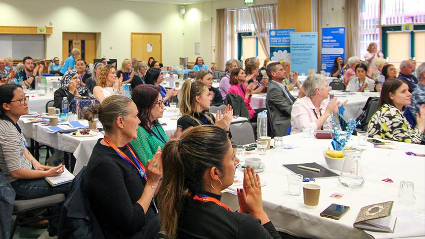 Several tables of people listening and clapping to speaker at Wakefield dementia roadshow event