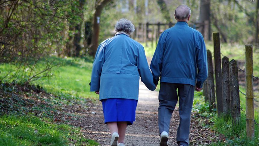 A couple walking down a country path and holding hands, they are both wearing blue clothes