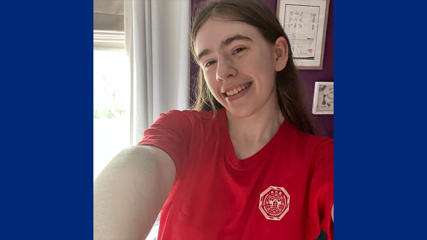 Eden has long brown hair, is smiling at the camera and wearing a bright red t-shirt