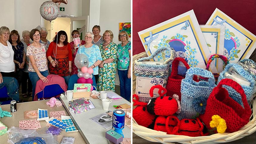 Members of the Charity Crafters Group stood by a table of crafting materials, and a basket of their knitted crafts