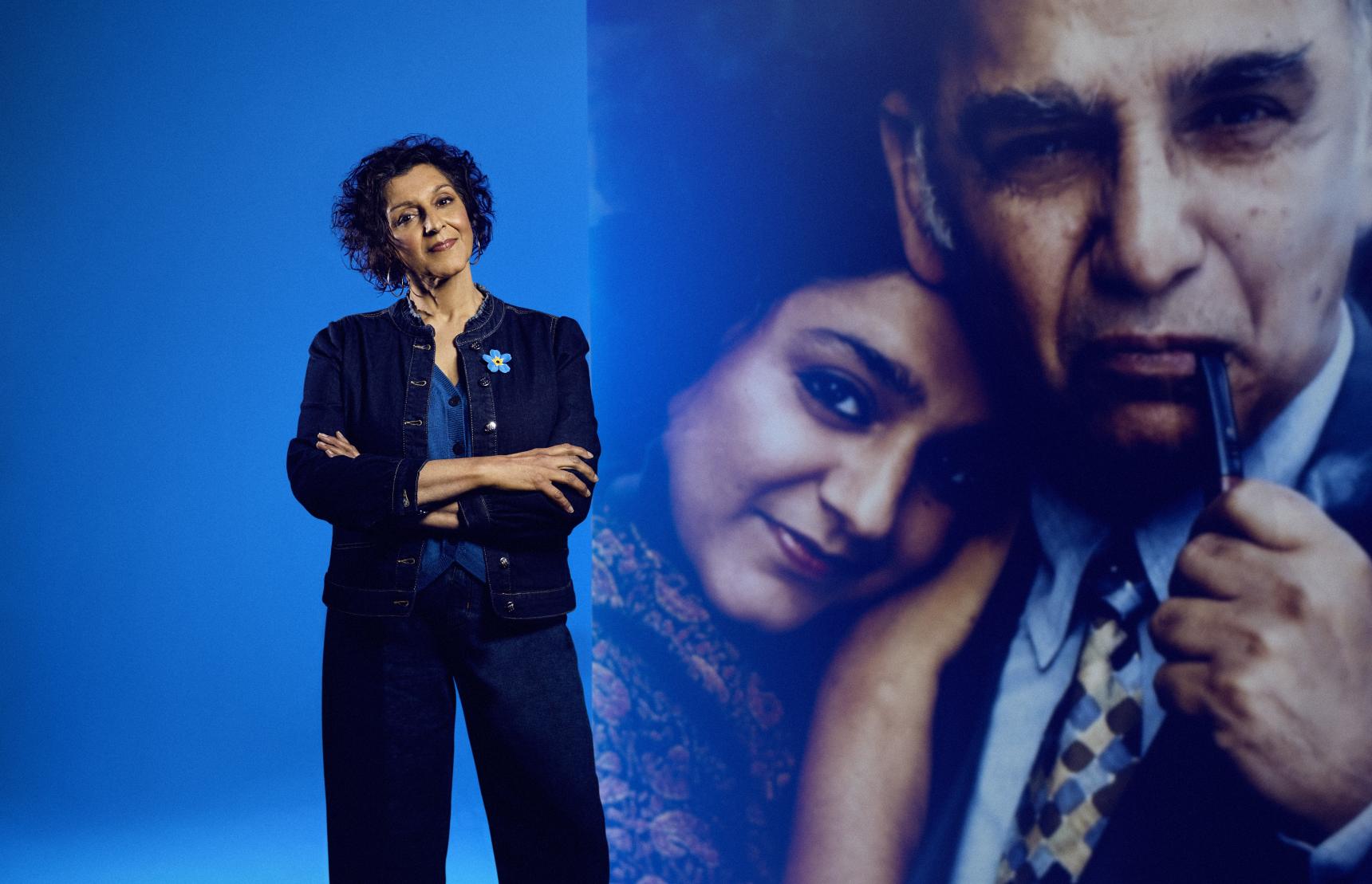 A woman stands in front of an enlarged photograph of her father