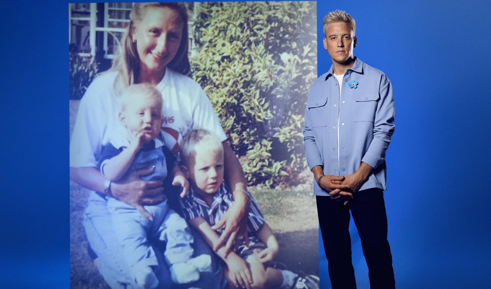 A man stands in front of an enlarged family photo, when he and his brother were just boys in the arms of their mum