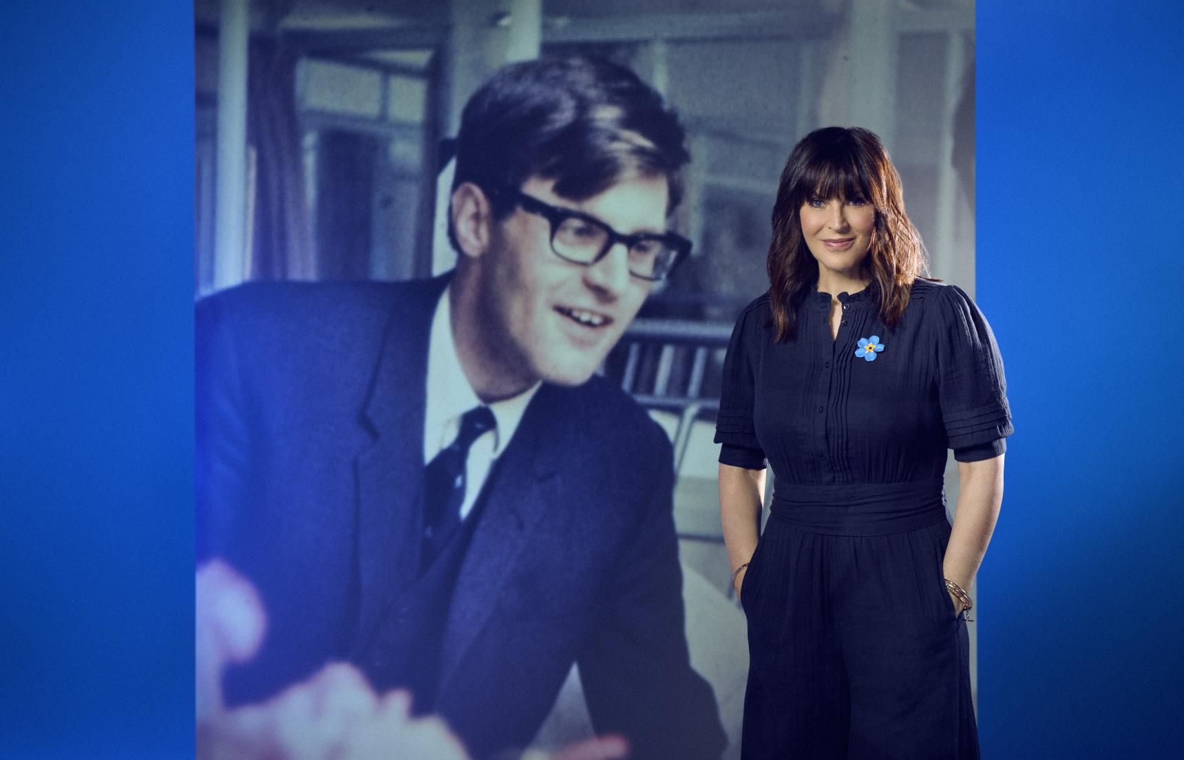 A woman stands in front of an enlarged photo of her father as a young man